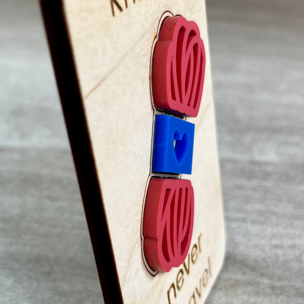 A side view close-up of a wooden magnet layered with a pink and blue acrylic skein of yarn, photographed against a gray textured background and designed to highlight the 3D effect of the yarn element.