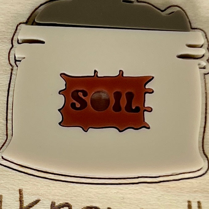 Close-up of I Know All the Dirt plant stake showing cream and red acrylic soil bag detail