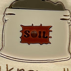 Close-up of I Know All the Dirt plant stake showing cream and red acrylic soil bag detail