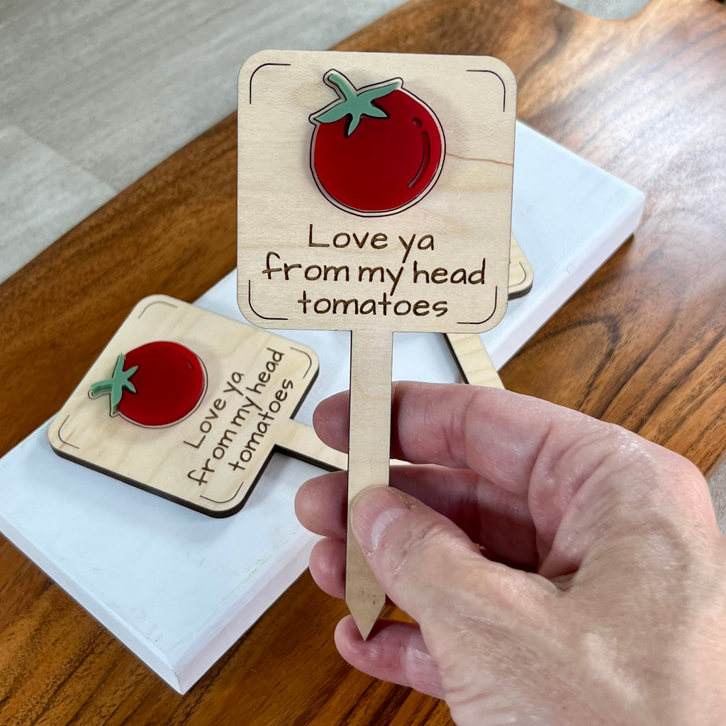 Hand holding Love Ya From My Head Tomatoes laser-cut maple wood plant stake with red acrylic tomato