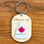 Elbows Up laser-engraved maple wood keychain with white acrylic toque and red maple leaf on wood background