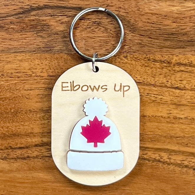 Elbows Up laser-engraved maple wood keychain with white acrylic toque and red maple leaf on wood background