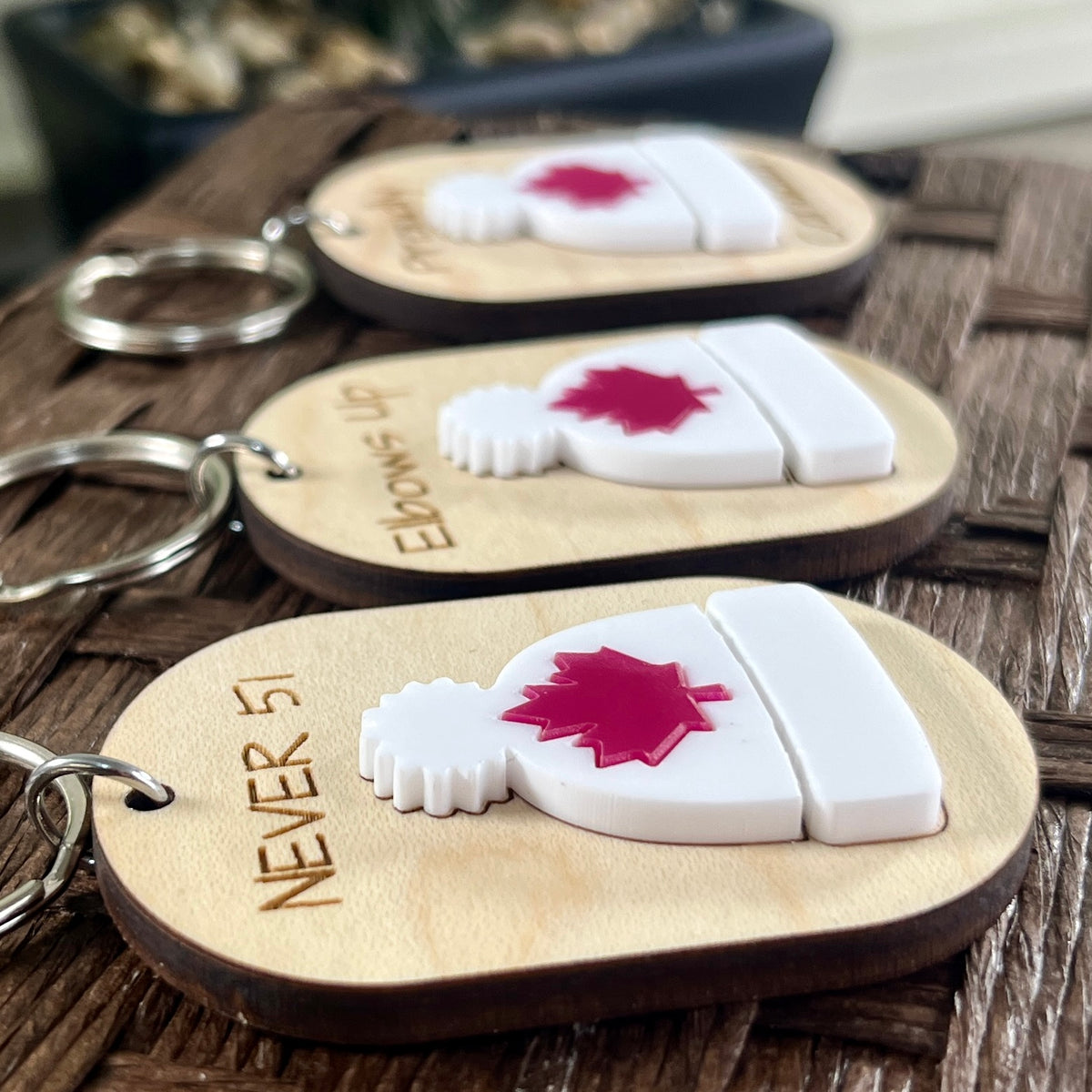 Three Never 51 toque maple keychains displayed on wood surface showing engraved text and white acrylic toque