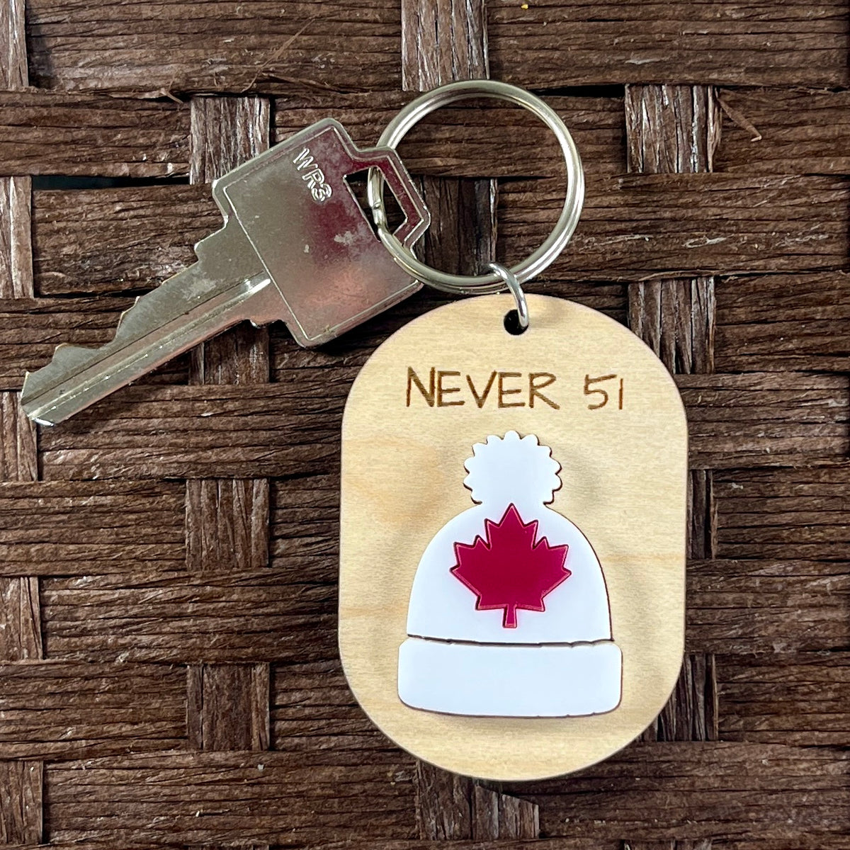 Never 51 toque maple keychains on wood surface with key ring attached showing red maple leaf detail