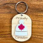 Proudly Canadian laser-engraved maple wood keychain with white acrylic toque and red maple leaf on wood background