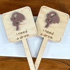 Two I Need a Drink laser-cut maple wood plant stakes with mauve acrylic wilted flower side by side