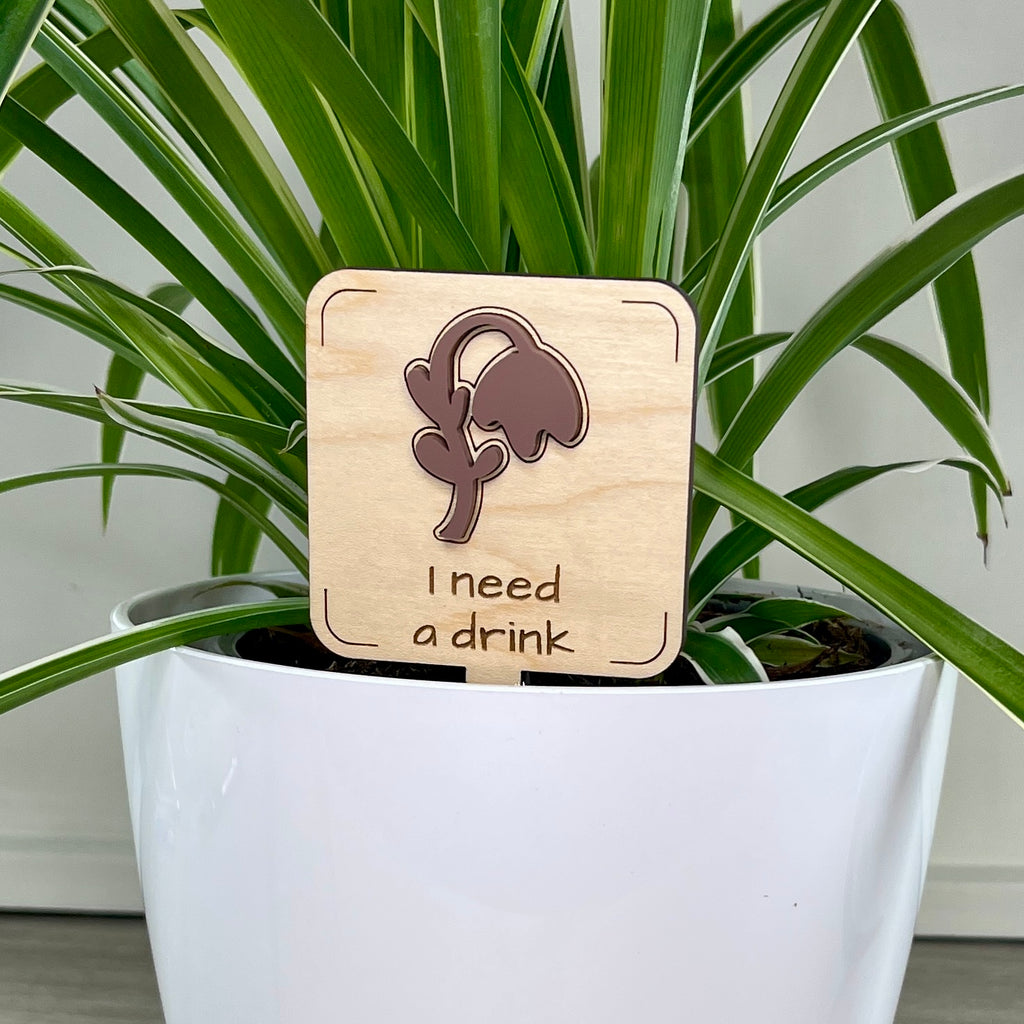 I Need a Drink maple wood plant stake with mauve acrylic wilted flower in a white pot