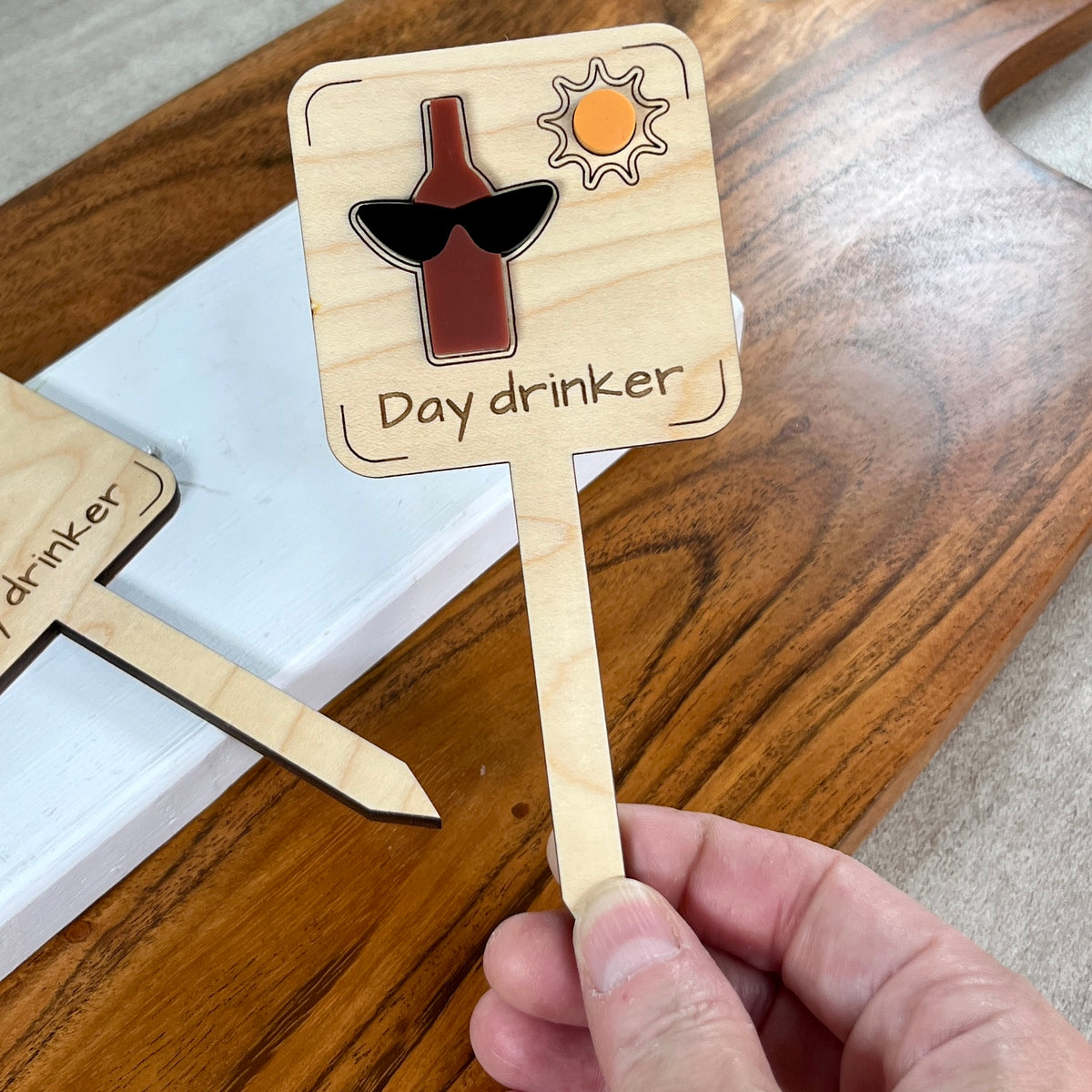Hand holding a Day Drinker laser-cut maple wood plant stake with wine bottle and sunglasses design