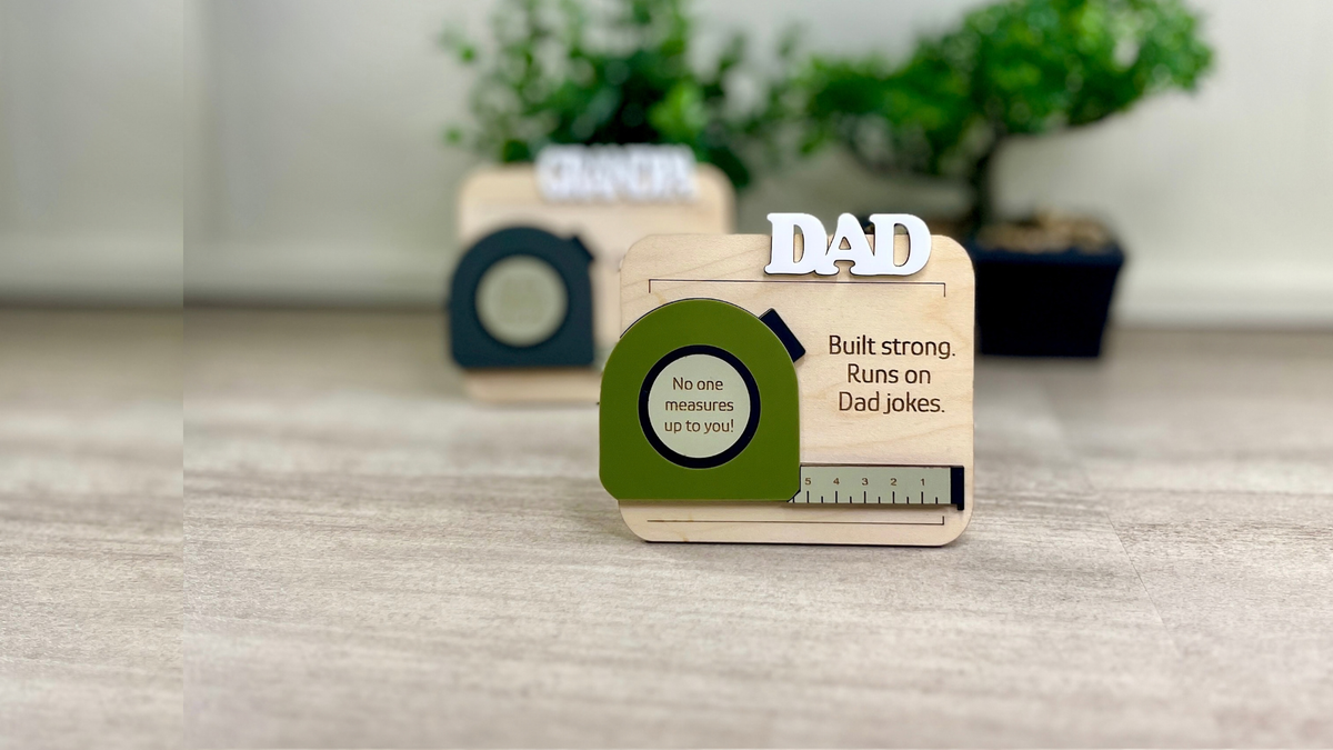 Wooden Dad gift with a green tape-measure design and the words ‘Built strong. Runs on Dad jokes.