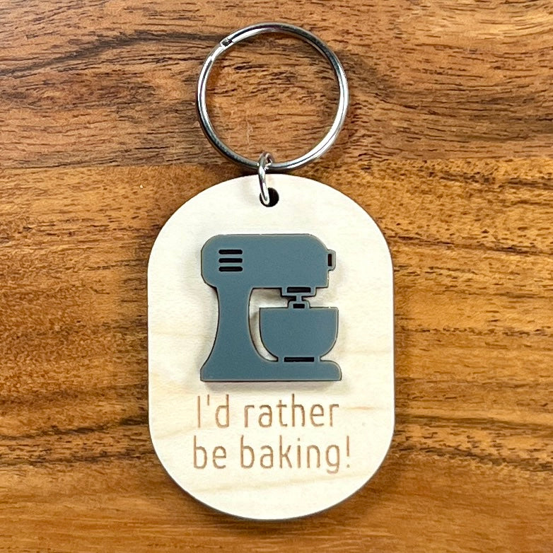 I'd Rather Be Baking laser-engraved maple wood keychain with grey acrylic stand mixer on wood background