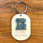 I'd Rather Be Baking laser-engraved maple wood keychain with grey acrylic stand mixer on wood background