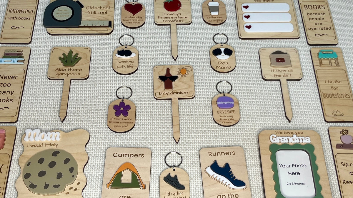 Assortment of illustrated wooden keychains, plant markers, and keepsakes displayed on a textured background